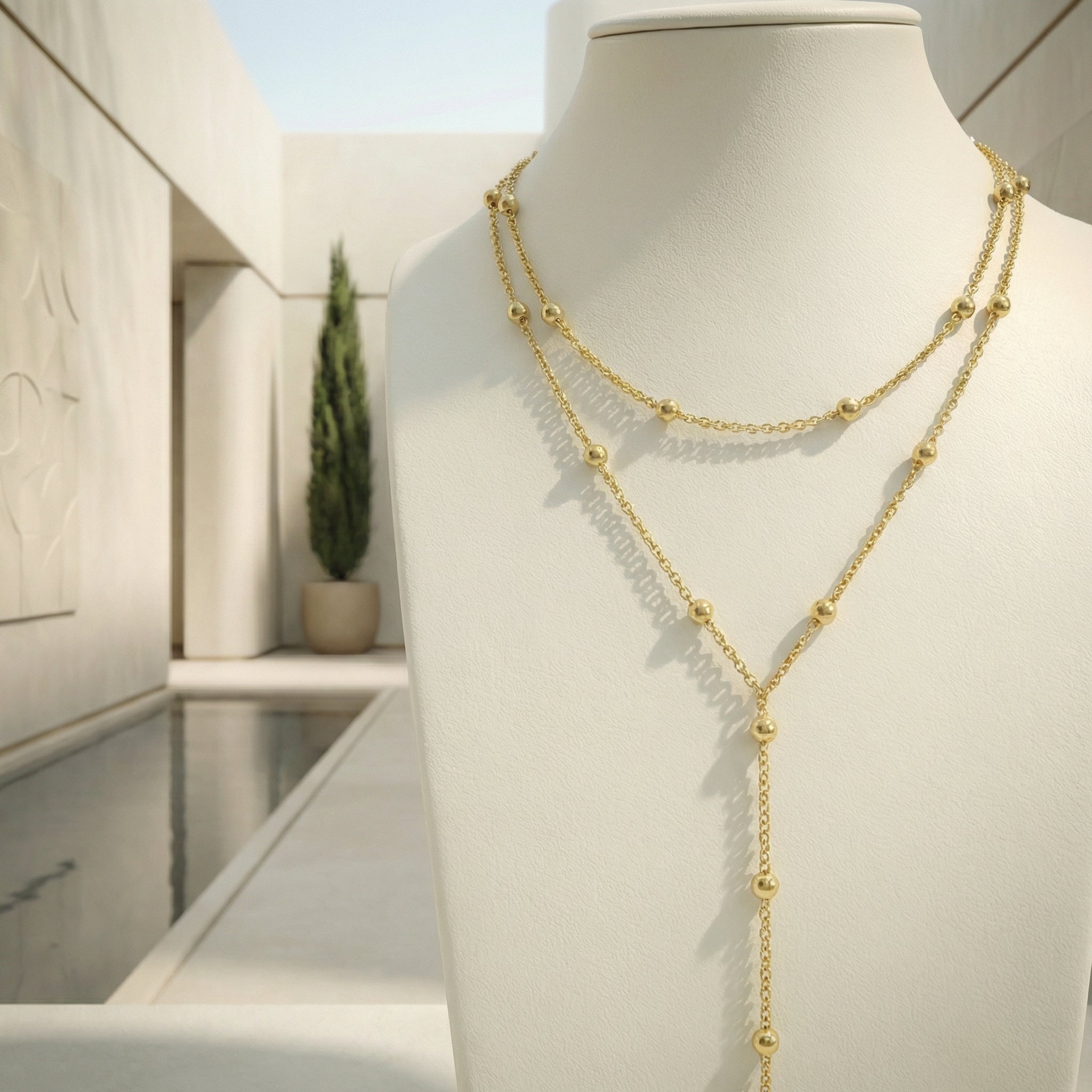 Dettaglio ravvicinato delle sfere lungo la catena e del pendente lineare in finitura oro